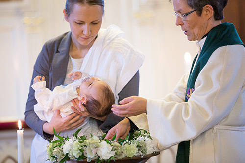 Pappi on laittamassa kättä lapseen ylle kastaakseen vauvan.